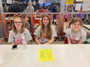 group of three young girls smiling as they volunteer for booksale