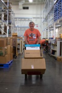 male volunteer smiling as he pushes a stack of boxes with a hand truck